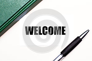 On a light gray background lies a pen, a green notebook and a white card with the text WELCOME. Business concept
