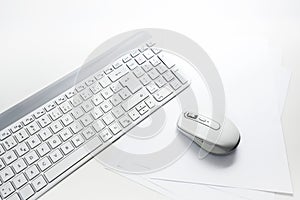 Light gray computer keyboard and mouse on blank paper and a white background with copy space, office concept, selected focus