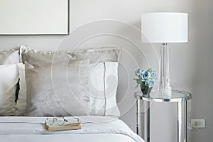 Light gray and white pillows on bed with flower jar on bedside table