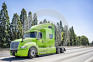 Light green big rig professional semi truck tractor driving on the wide multiline highway road to warehouse for pick up loaded
