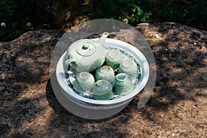 Light green ceramic tea set including jar, cups and plate on stone table under tree shadow at Ham Rong Mountain Park in Sa Pa