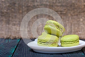 Light green macarons lie on a saucer. On pine planks with a crisp woody texture