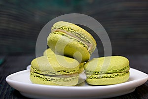 Light green macarons lie on a saucer. On pine planks with a crisp woody texture