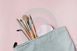 A Light Green makeup cosmetic bag with cosmetic beauty tools and product spilling out on to a pastel colored pink background Top