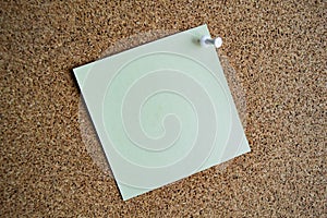 A light green paper note on a cork board, attached with a white pushpin. Copy space