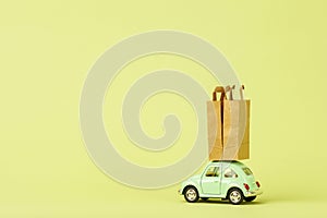 Light green retro toy car carries paper shopping bags. Eco goods delivery concept