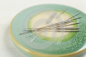 Light green stone coaster with acupuncture needles on white table, closeup