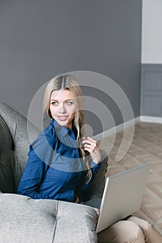 Light-haired woman with a laptop sitting in an armchair