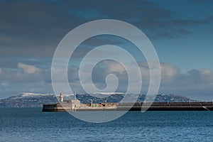 The light house in dun laoghaire harbour with hill of Howth cover by snow, Ireland