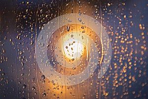 Light of a lantern and rain drops on the window. Abstract blurred background