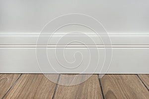 Light matte wall, white baseboard and tiles immitating hardwood flooring