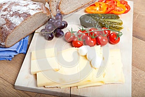 Light meal on rustic wooden board with german bread, cheese, mozzarella, fruits and vegetables