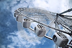 Light metal cabins of ferris wheel with booths with windows against blue sky, bottom view