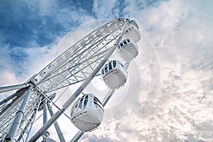 Light metal cabins of ferris wheel with booths with windows against cloudy sky, bottom view