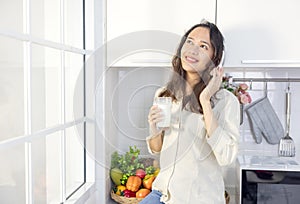 In a light modern kitchen, a beautiful woman drinks milk while listening to music. Before breakfast, she`s having a good time and