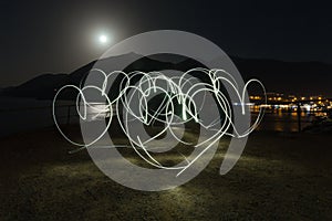Light painting heart shapes over mountains, sea and night town background. Love.