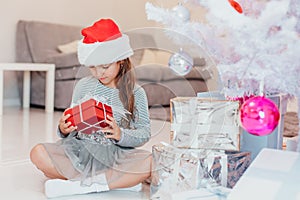 Light photo of cute kid sitting with gift in hands, like a little gnome in christmas decorated room.