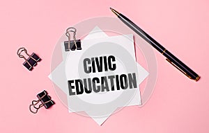 On a light pink background, black paper clips, black pen and white note paper with the words CIVIC EDUCATION. Flat lay