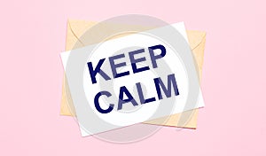 On a light pink background - a craft envelope. It has a white sheet of paper that says KEEP CALM