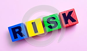 On a light pink background, multi-colored wooden cubes with the text RISK