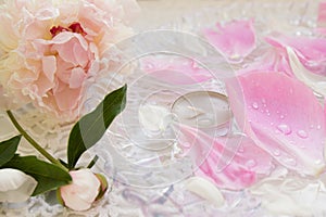 Light pink flower peony with bud rests on a white table groa with a glass dish with peony petals and a candle