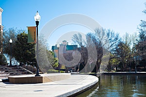 Light pole banner and buildings along Bricktown canal with curved sidewalk pathway, riverside restaurants, tourist attractions in photo