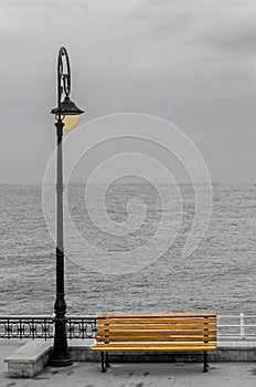 Light pole with colored bench on seafront, seaside, cloudy day, dawn