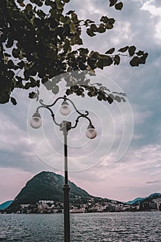 A light pole near the wavy sea with the background of green mountains under breathtaking cloudy sky