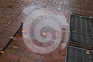 Light reflecting in puddles on wet red brick sidewalk, metal grates and autumn leaves