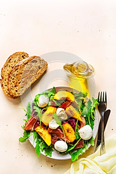 Light salad of fresh peaches, parma ham, mozzarella and green salad mix, olive oil, bread, fork and knife