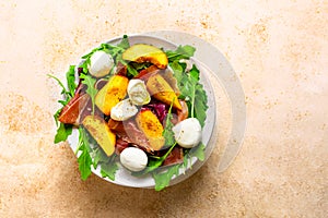 Light salad of fresh peaches, parma ham, mozzarella and green salad mix on peach colored background