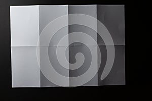 Light and shadow on creases in sheet of white paper folded into eight equal sections, on black