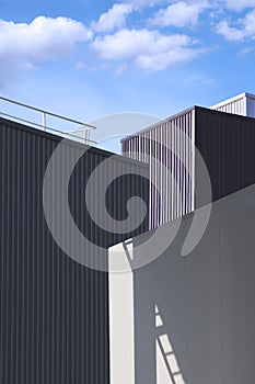 Light and shadow on surface of cold storage room with corrugated metal industrial buildings against clouds on blue sky