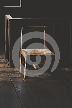 Light and shadow on surface of the old empty wooden chair near the railing inside of traditional wooden house in dark tone style