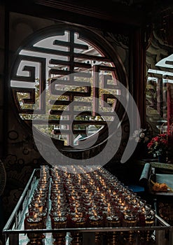 Light shines through Chinese-style circular window with Many red votive candles light