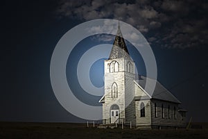 light shining on old country church at night time.