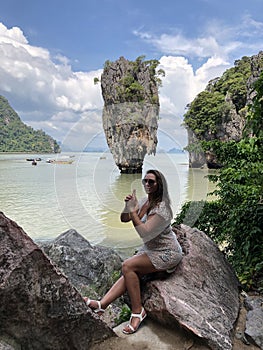 A light-skinned girl in beach clothes folded a gun from her fingers on the famous picturesque James bond island in Thailand, in
