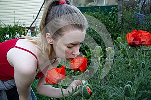 Light-skinned girl with freckles in a red top sniffs on the street big red poppies