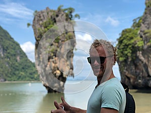 A light-skinned guy in sunglasses and a t-shirt shows his fingers the sign perfectly on the famous James bond island in Thailand,