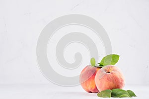 Light soft summer modern kitchen interior with two ripe peaches with green leaf on white wood table, copy space.