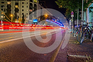 light streams from passing vehicles reflecting off tram lines down center of road and hire bikes on right.