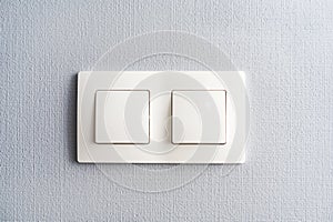 A light switch, a plastic mechanical switch of white color installed on a light gray wall in the room