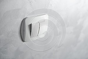 Light switch, a plastic mechanical switch of white color installed on a light gray wall.