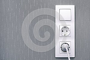 Light switch , power sockets, lead and plug on gray wall