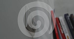 Light switch on a white wall, blurred books in the background.