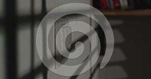 Light switch on a white wall, blurred books in the background.