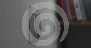 Light switch on a white wall, blurred books in the background.