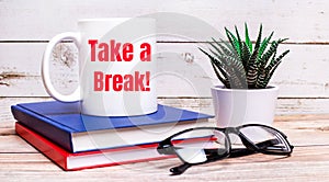 On a light table are notepads, a potted plant, black-framed glasses and a white cup with the text TAKE A BREAK