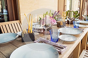 Light Table set for wedding or another catered event dinner. Wooden table served with plates, forks, spoons, glasses, napkins in t