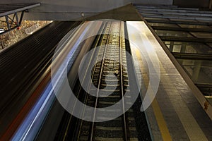 Light trail of quickly driving metro train at night in Athens, Greece with a platform and second railroad